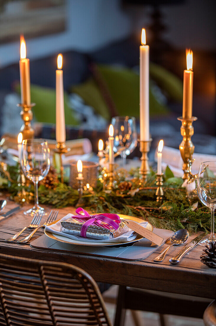 Christmas present at place setting with lit candles and foliage in Norfolk cottage England UK