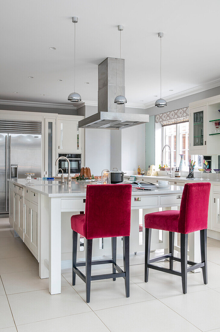 Barhocker aus rotem Samt an einer Kücheninsel mit Edelstahldunstabzug in einem Haus in Hampshire UK
