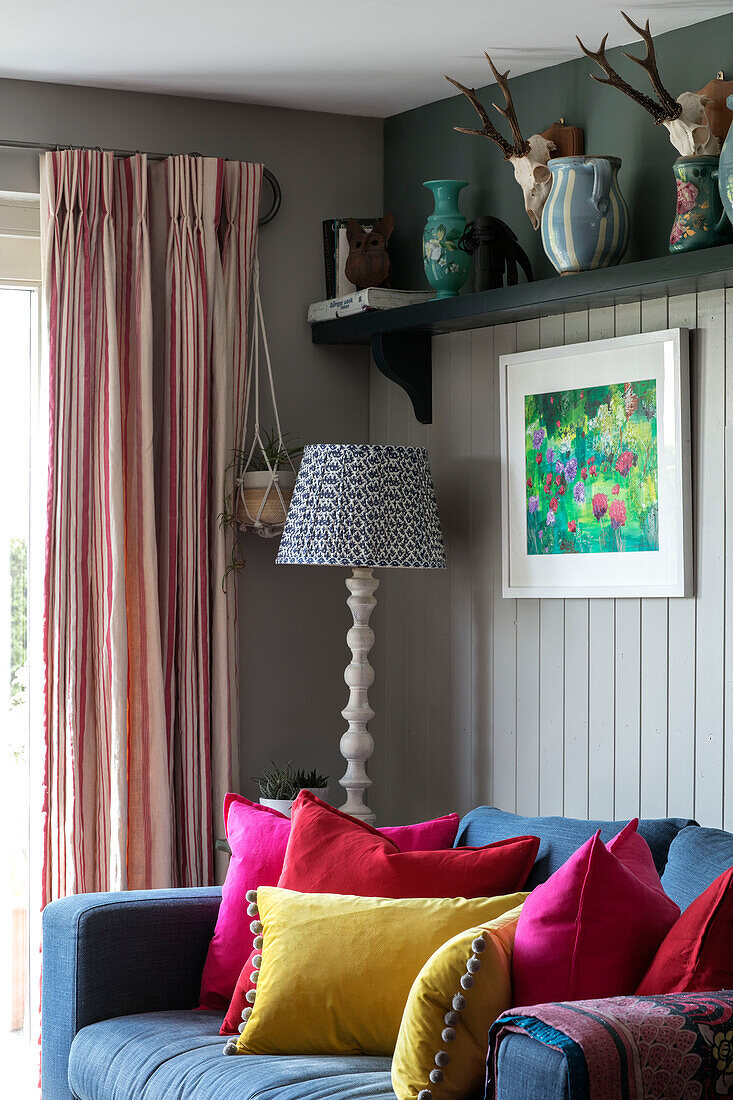 Graues Sofa mit hellen Kissen und gestreiften Vorhängen unter einem Regal in einem Haus in Hampshire, England, Vereinigtes Königreich