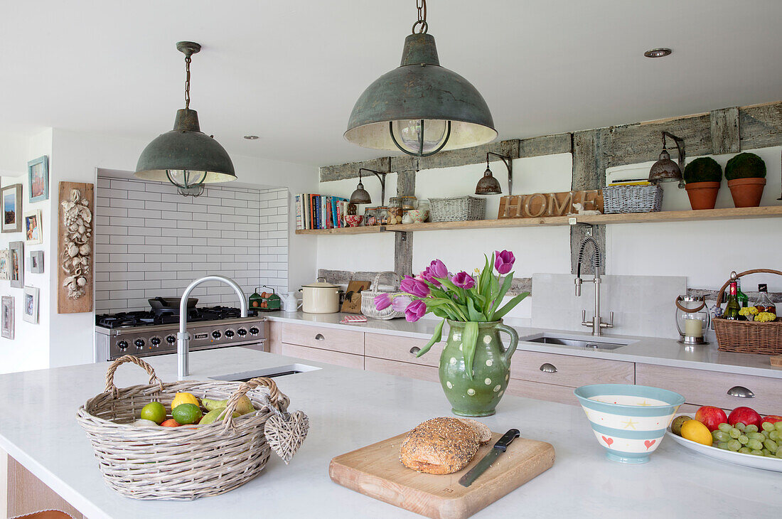 Industrielle Pendelleuchten über der Kücheninsel mit Tulpen und Obstkorb in einem Bauernhaus in Surrey UK