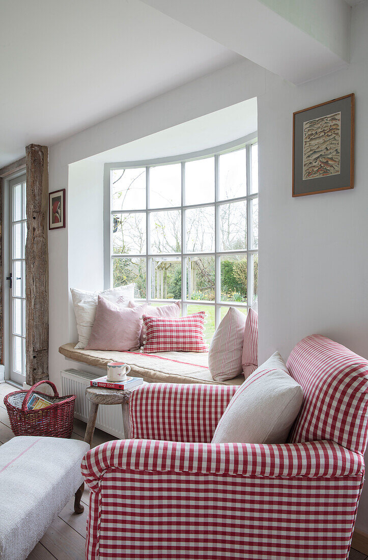 Bay window seat and antique armchair in red check with wicker basket in Surrey farmhouse UK
