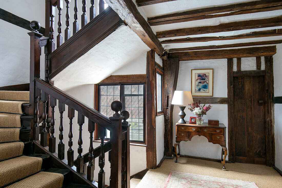 Antique side table and lamp with wooden banisters in staircase landing of timber framed Kent farmhouse UK