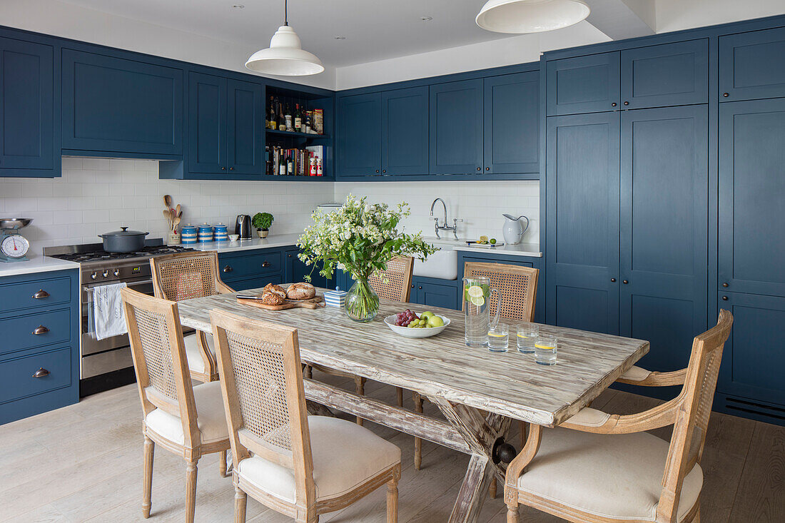 Tisch aus alten Gerüstplanken mit blauen Elementen und Korbstühlen in der Küche einer Wohnung im Norden Londons UK