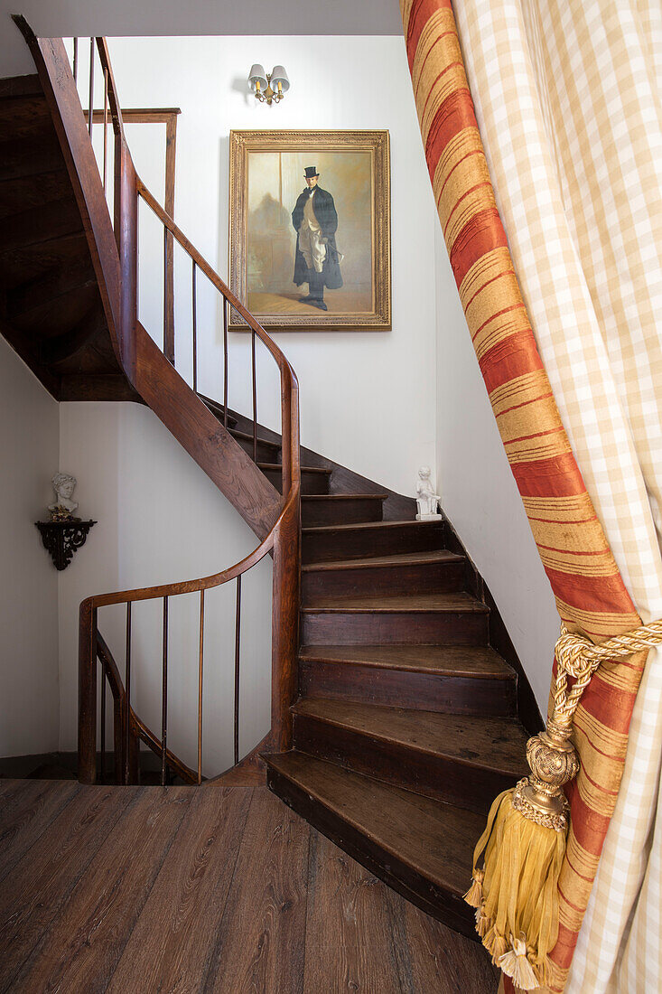 Gestreifte goldene Türvorhänge und Holztreppe mit gerahmtem Porträt in einem Stadthaus in Issigeac im Perigord, Frankreich