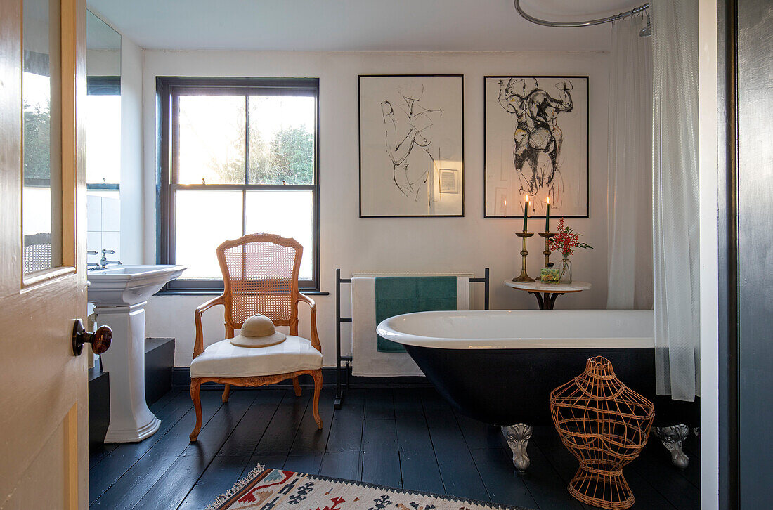 Pencil sketches and wicker chair with black bath and painted floorboards in Norfolk farmhouse UK