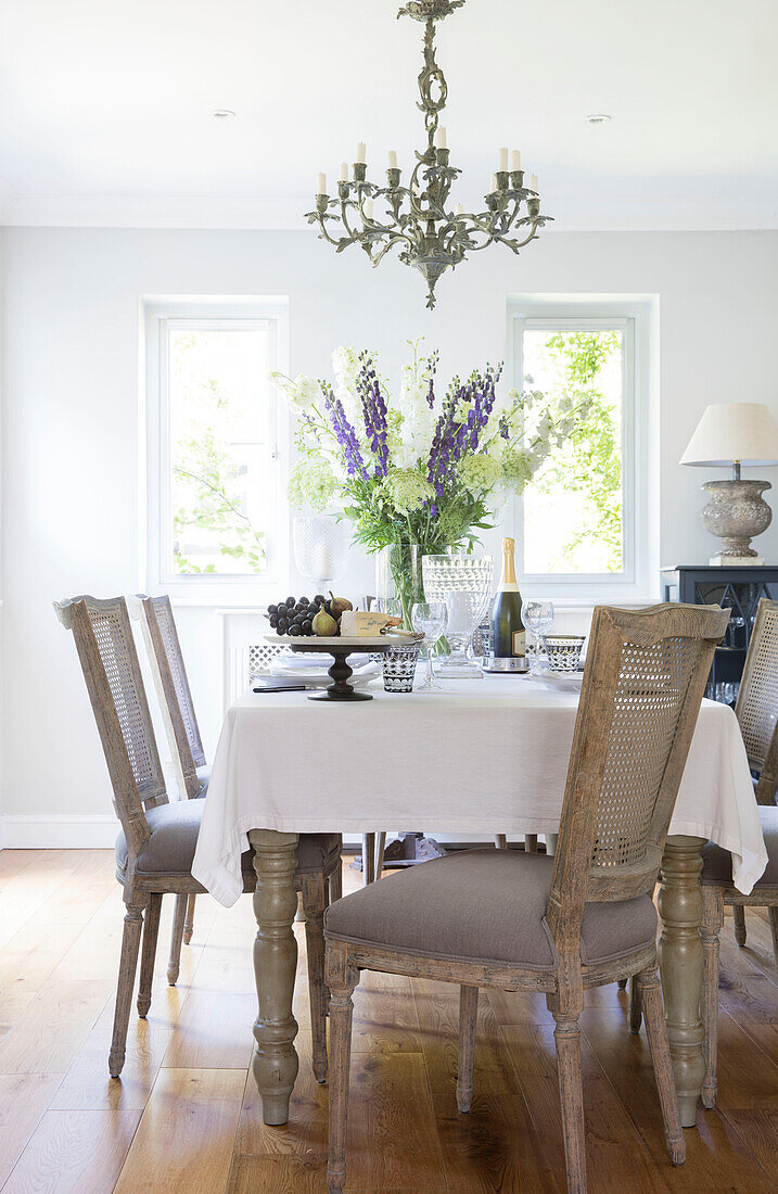 Wisteria in windows of dining room with cane-backed chairs at table walls in Ammonite Surrey cottage UK