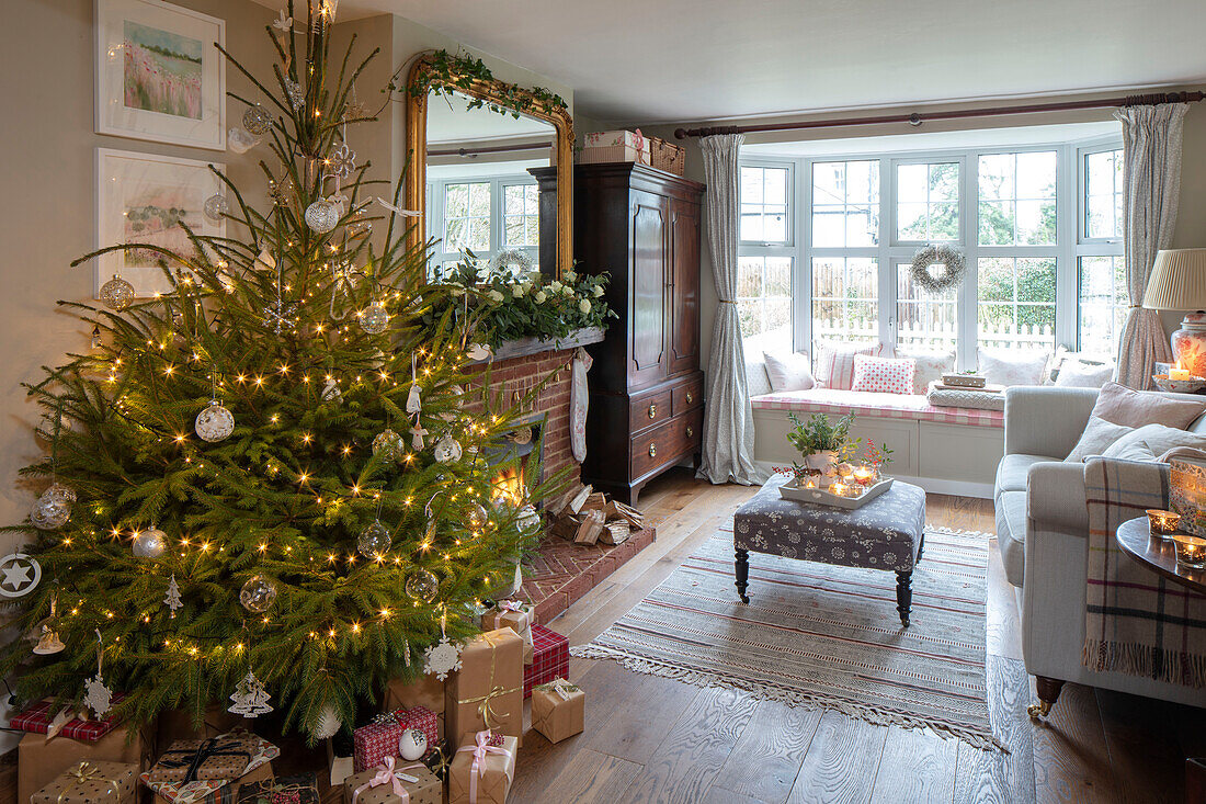 Christmas presents under tree with covered footstool and window seat in Hampshire cottage UK