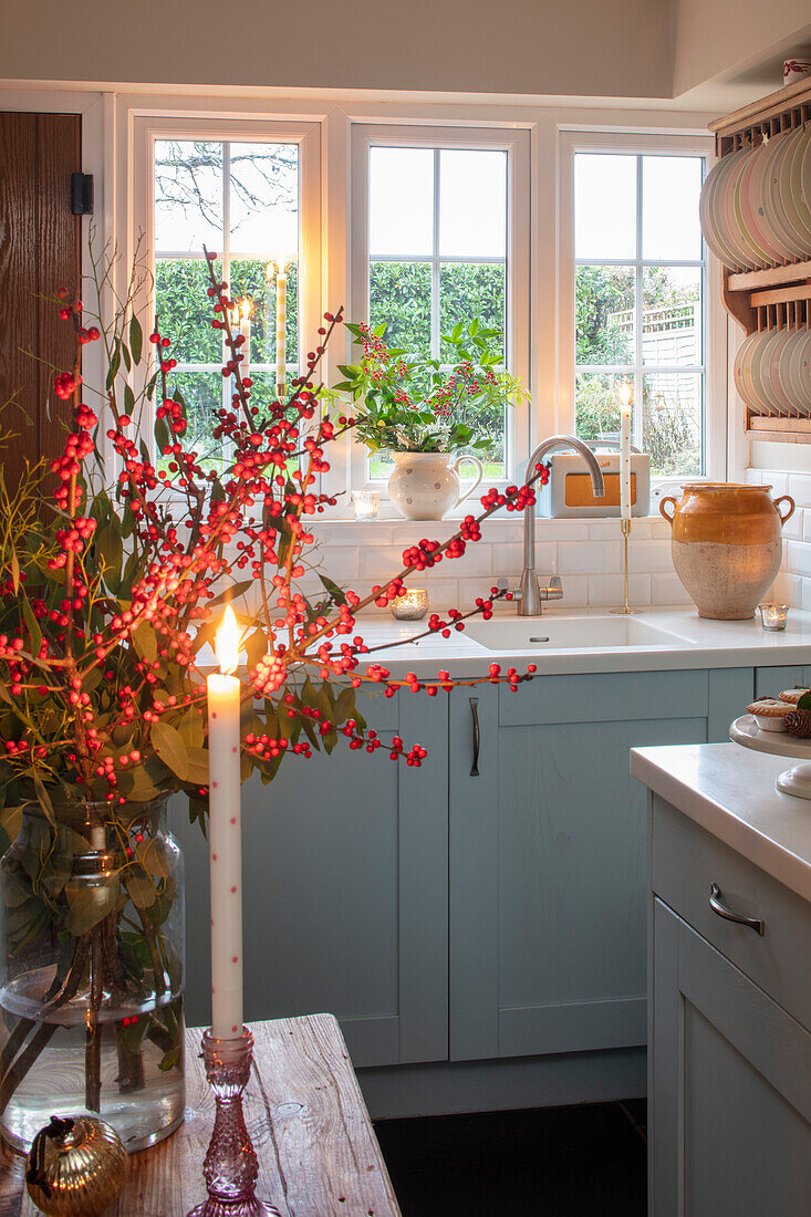 Beleuchtete Kerze und Beeren in einer puderblauen Küche in einem Cottage in Hampshire, Großbritannien