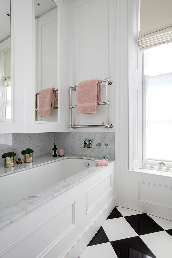 Pinkes Handtuch auf einer Stange über der Badewanne mit Spiegelschränken in einem Londoner Stadthaus UK