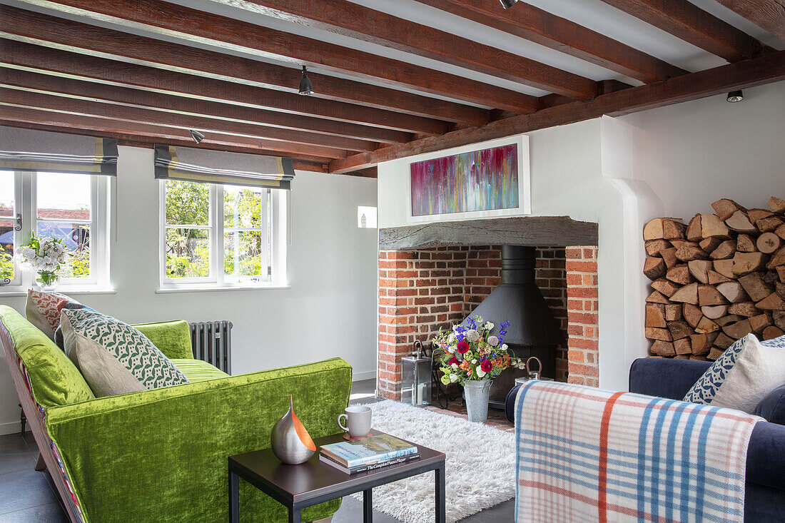 Grünes Sofa mit Kaminholz und offenem Ziegelsteinkamin Surrey UK