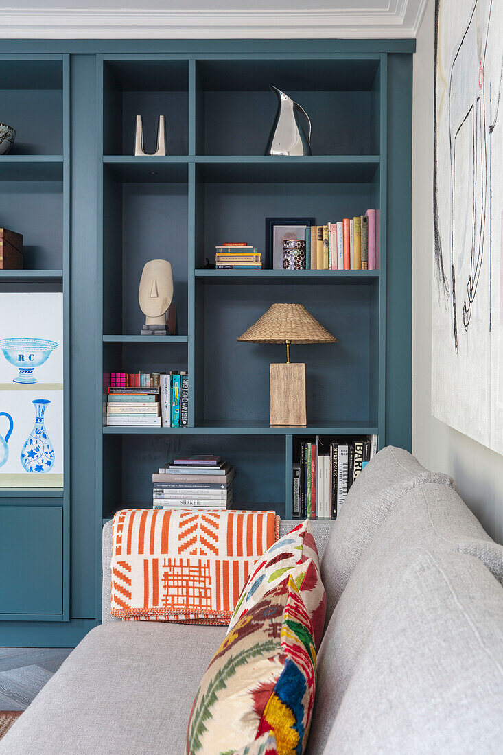 Ornaments and books on teal shelving with linen sofa London UK
