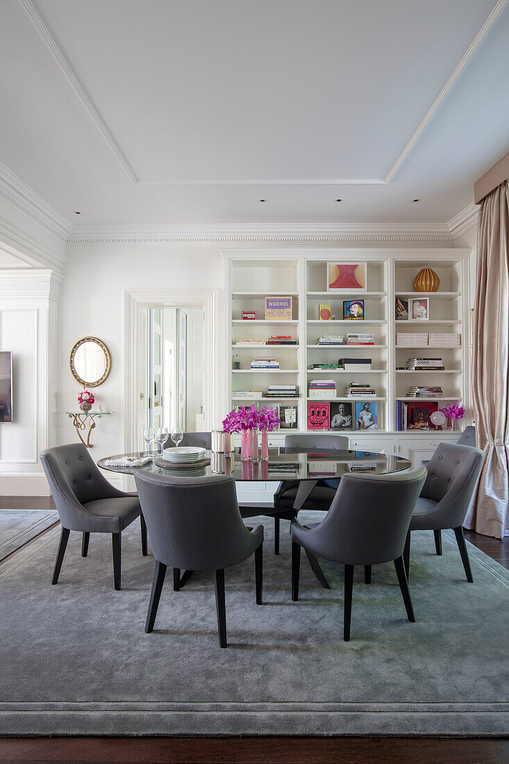 Grey dining chairs at oval table with bookshelf in London townhouse UK