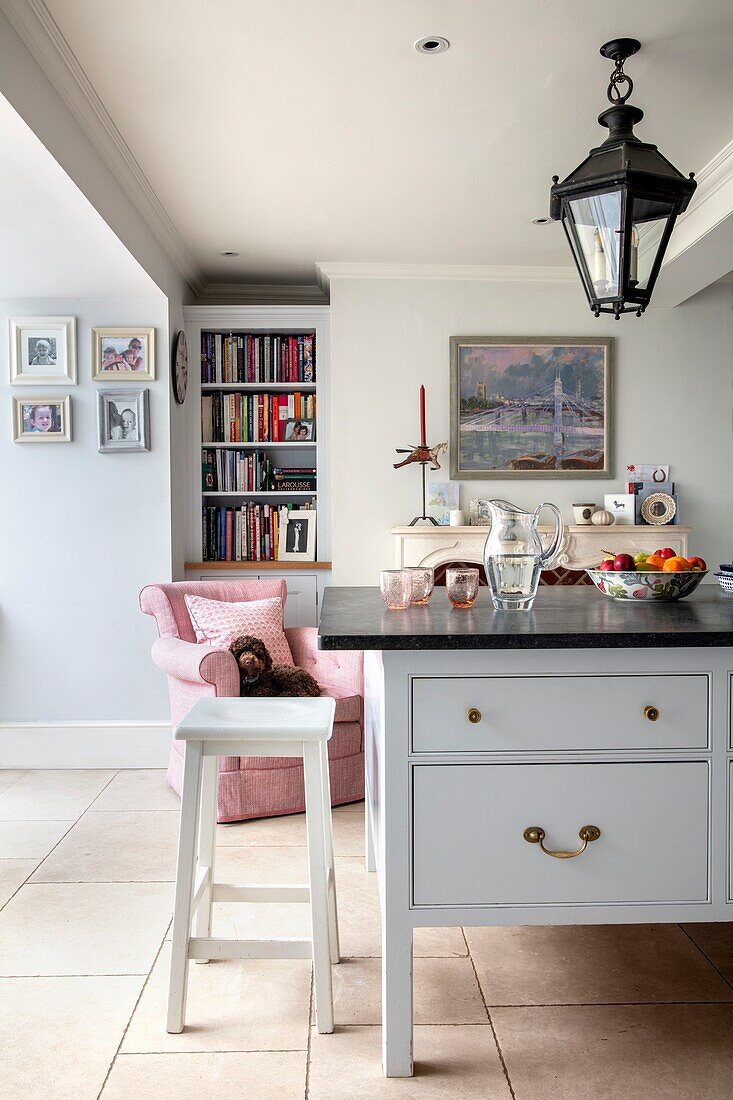 White and pale blue kitchen with dark grey worktop and pale pink armchair with dog in elegant Hampshire home UK