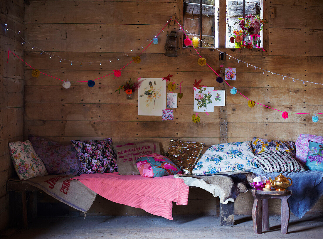 Verschiedene Kissen auf einer Sitzbank unter dem Fenster in einer rustikalen Holzhütte im Herbst UK