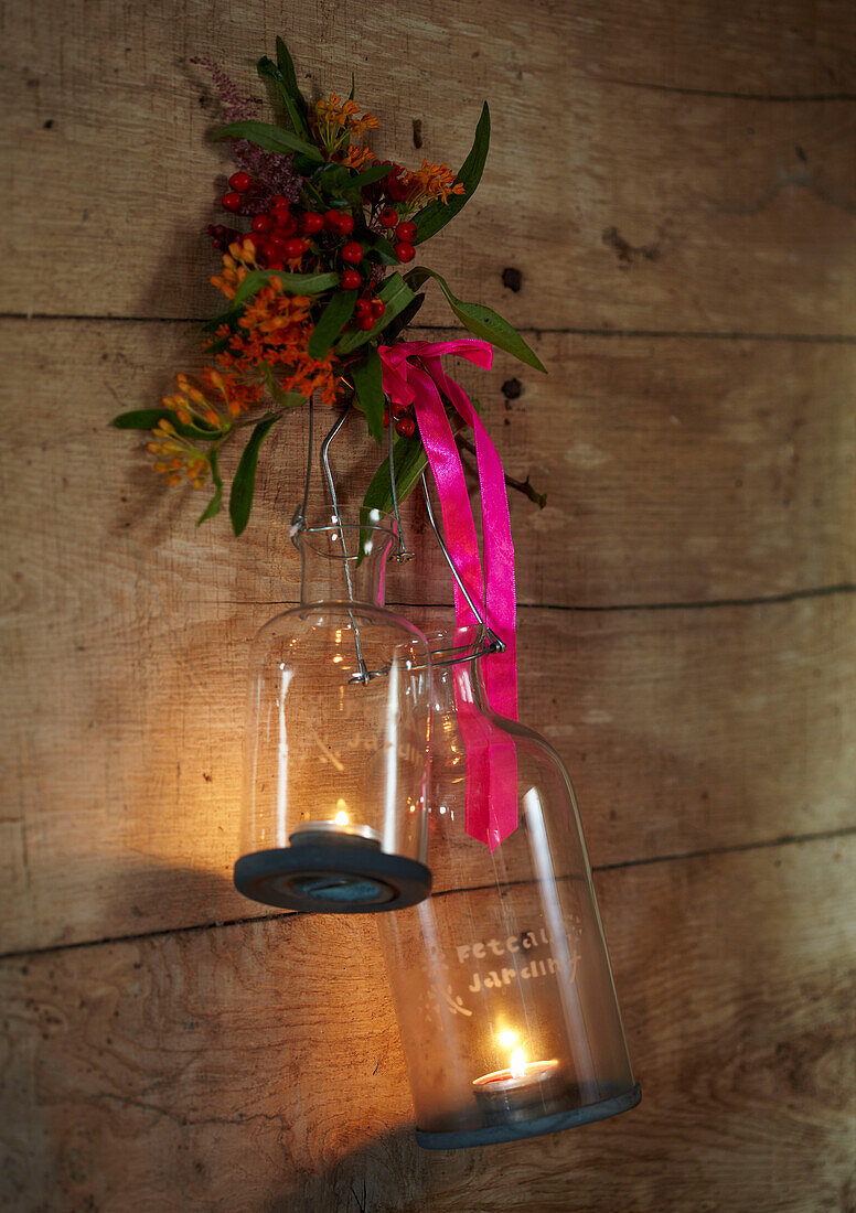 Glass candle holders hang with pink ribbon in rustic wood cabin Autumn UK