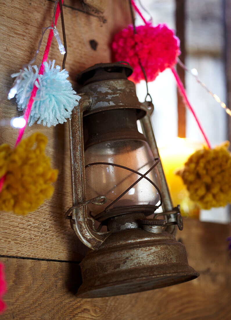 Rusty hurricane lantern and pompoms in wood cabin UK