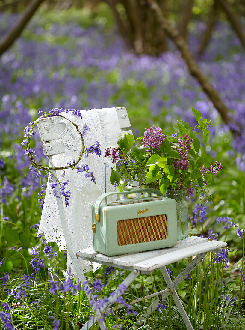 Vintage-Radio auf einem Klappstuhl mit Schnittblumen in einem Blauglockenwald (Hyacinthoides non-scripta)
