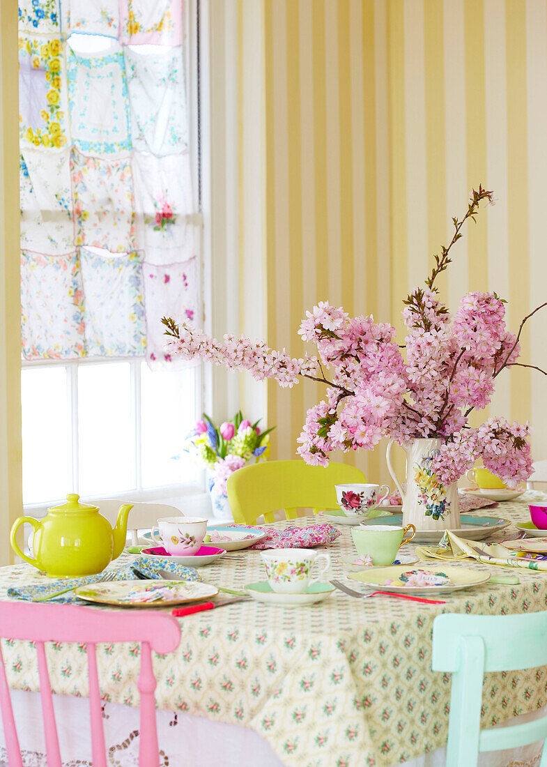 Pink blossom and yellow teapot on table set for afternoon tea