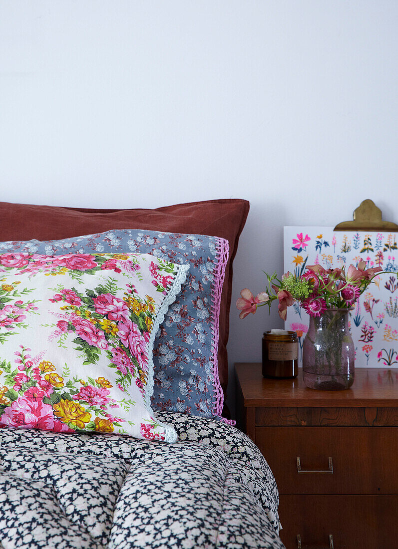 Vintage-Bettwäsche mit spitzenbesetzten Kissen und Vase mit frischen Blumen auf dem Nachttisch