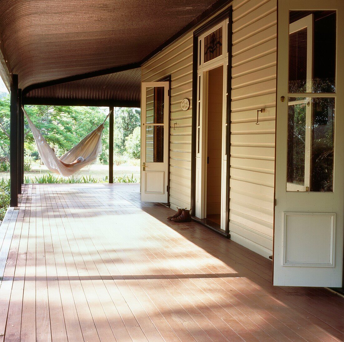 Holzgetäfeltes Haus im kolonialen Landhausstil mit großer Veranda, französischen Fenstern und einer Hängematte im gedämpften Sonnenlicht