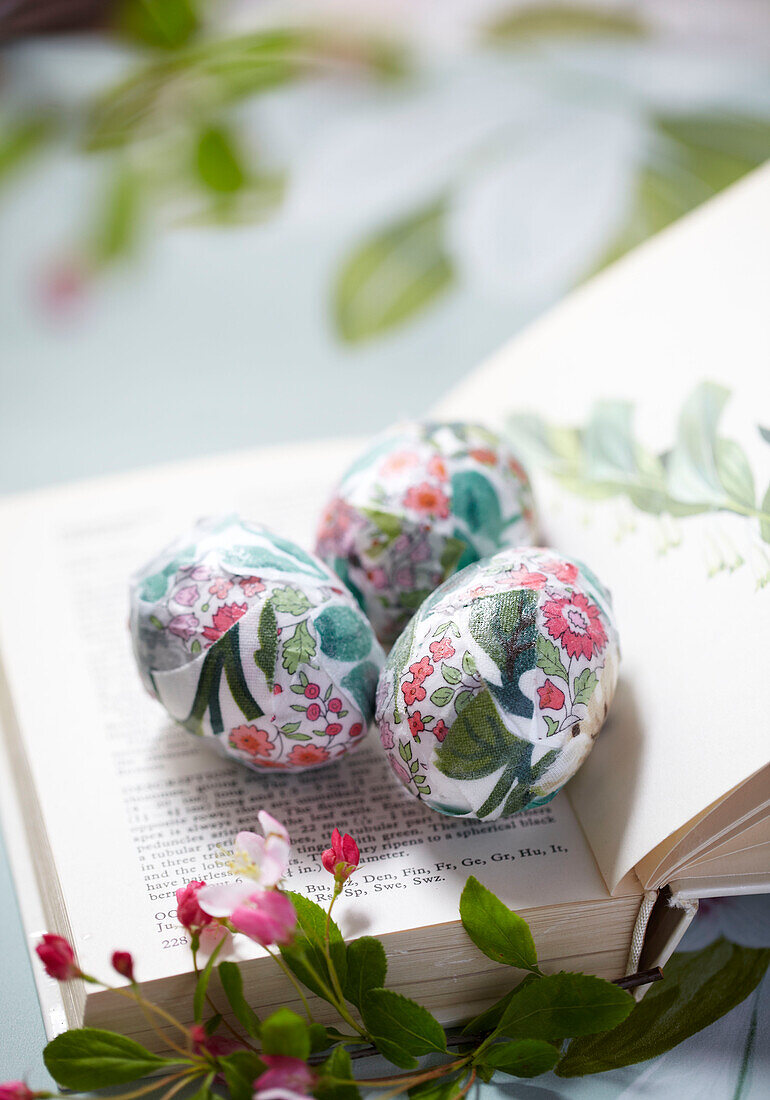 Open book on table with three eggs wrapped in floral fabric