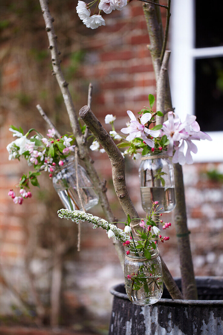 Frühlingshafte Blumendekorationen im Freien aus mit Blüten gefüllten Marmeladengläsern als Vorbereitung für ein Osterfest