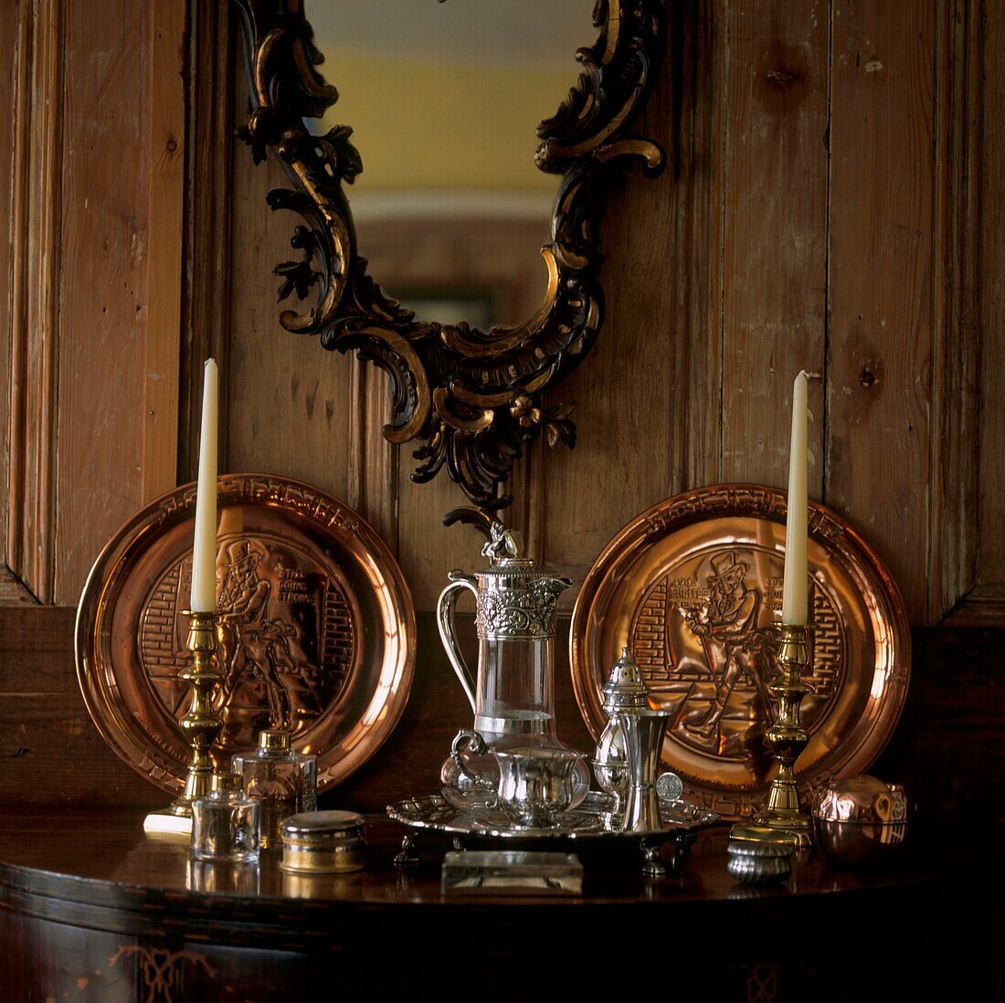 Antikes Silber- und Messinggeschirr auf Tischplatte mit Holzvertäfelung und verziertem Spiegel