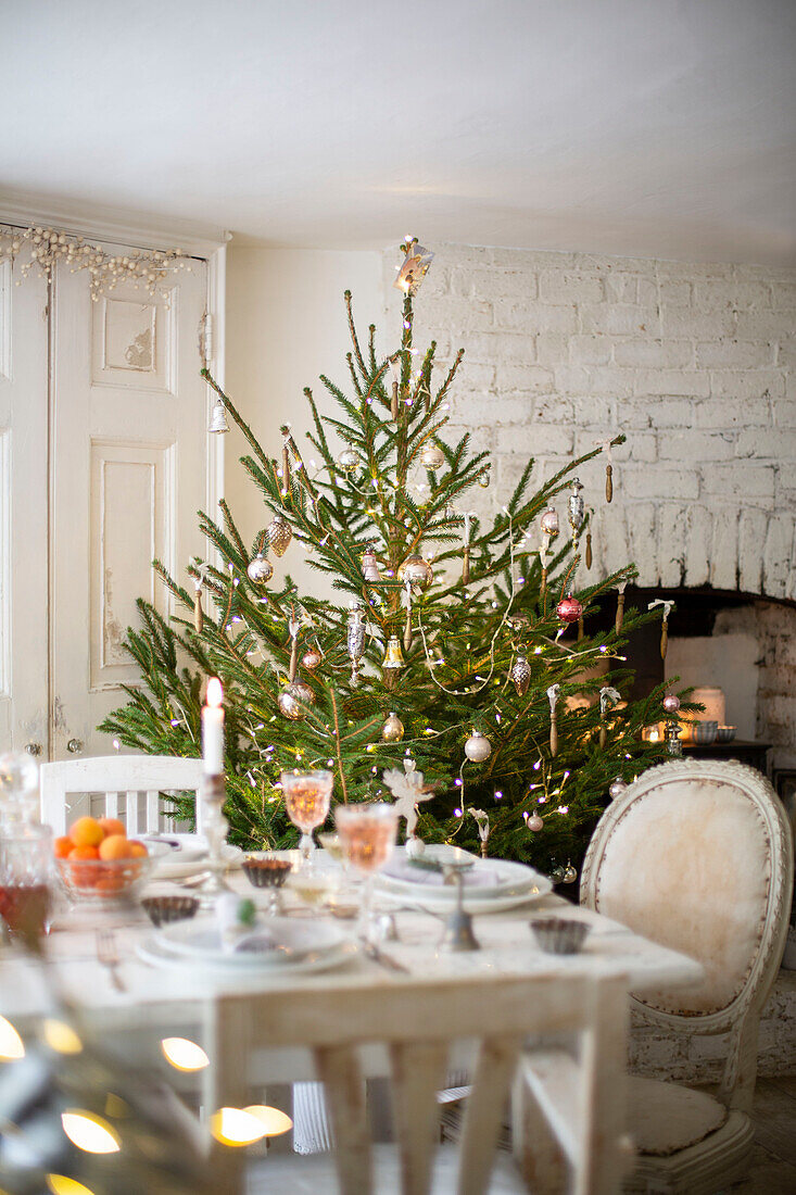 Festive table setting in dining room with decorated Christmas tree and lit candles