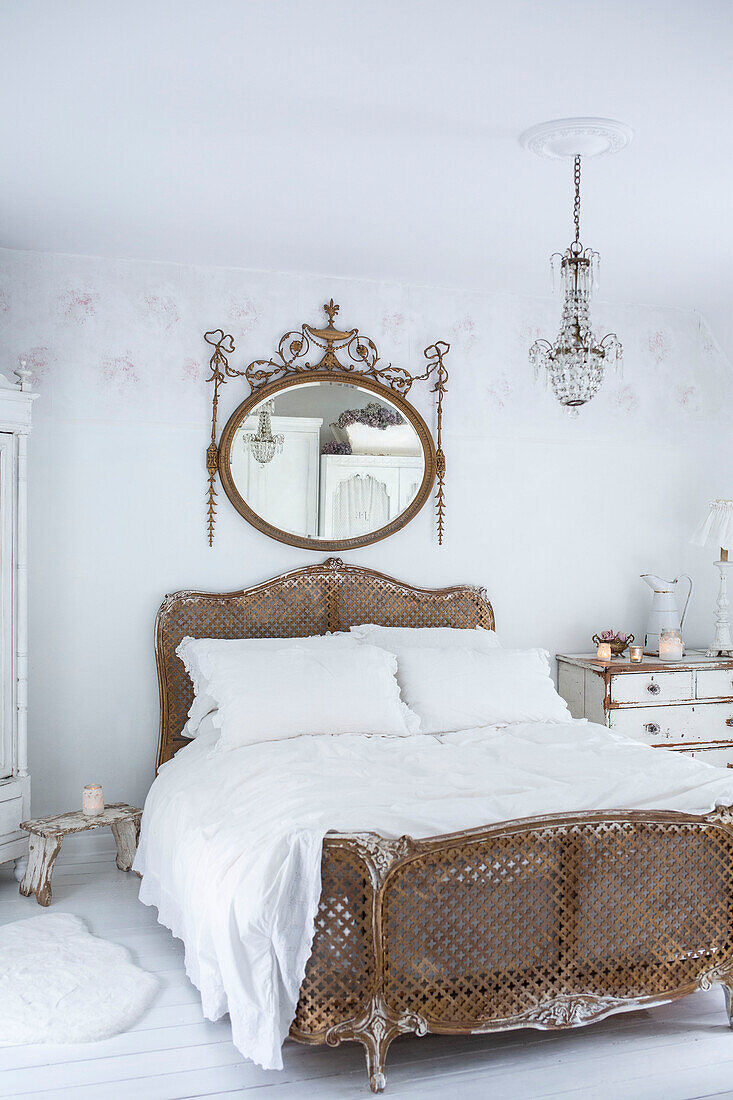 Scandinavian style bedroom with distressed paintwork and vintage bed and chest of drawers and large Louis IV style gilt mirror