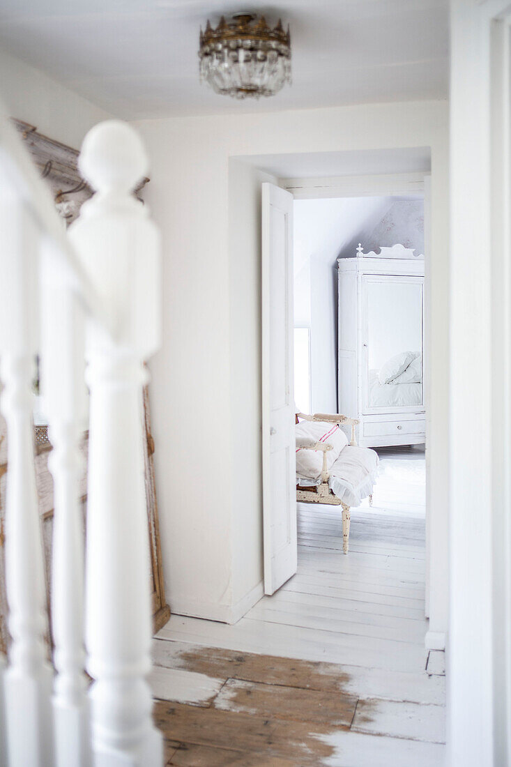 Blick durch die Schlafzimmertür auf einen weiß gestrichenen, verspiegelten Kleiderschrank und einen alten Stuhl auf gestrichenen Dielen
