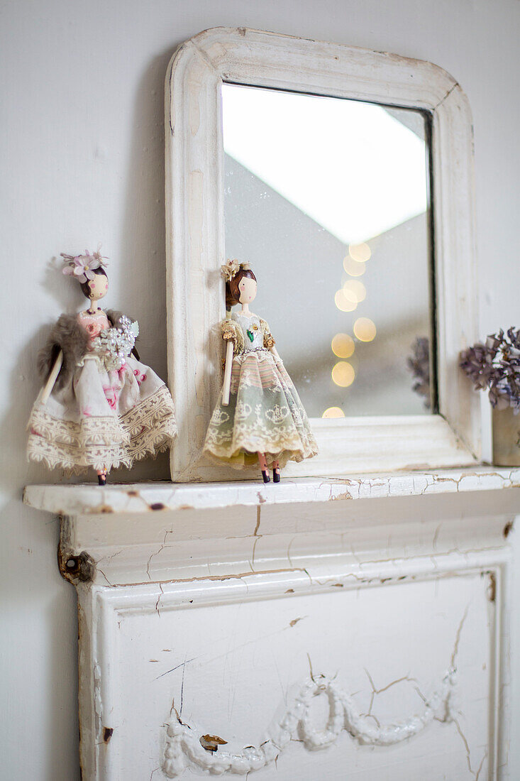Detail of vintage dolls on white painted mantlepiece with mirror reflecting the skylight in attic bedroom