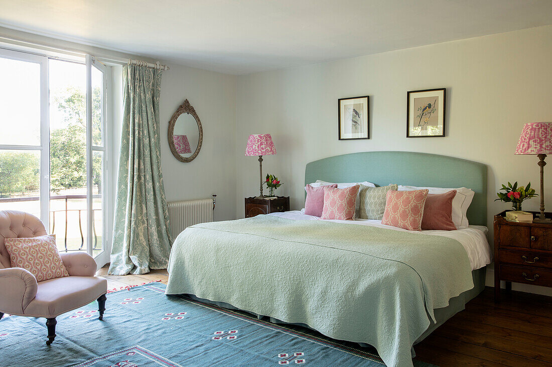 Doppelbett mit Kissen, antike Nachtschränke und rosa Sessel im Schlafzimmer