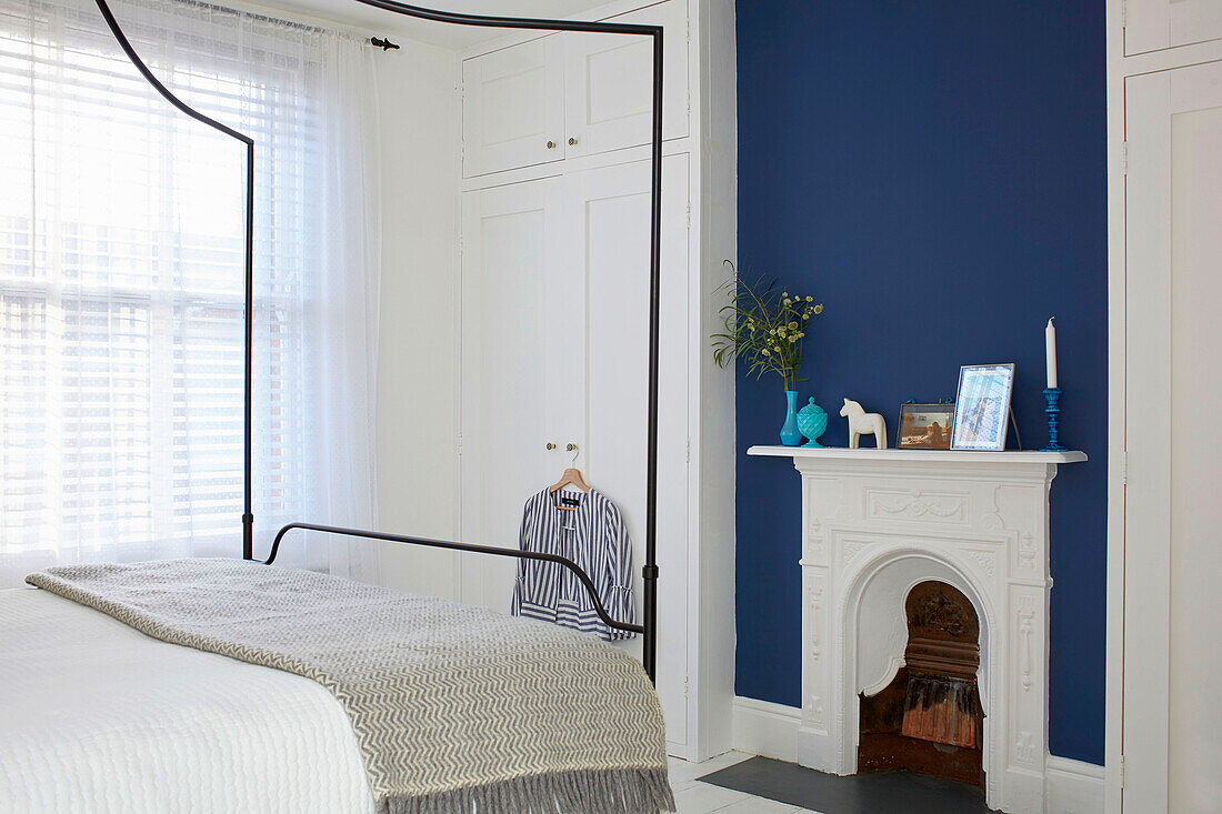 Queen bed with canopy, white floor-to-ceiling built in wardrobe and fireplace against blue wall in bedroom