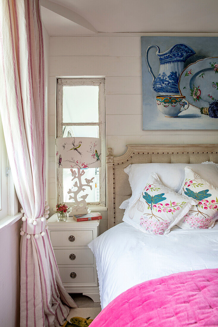 Bedroom with white bedside table, pink blanket and floral cushions