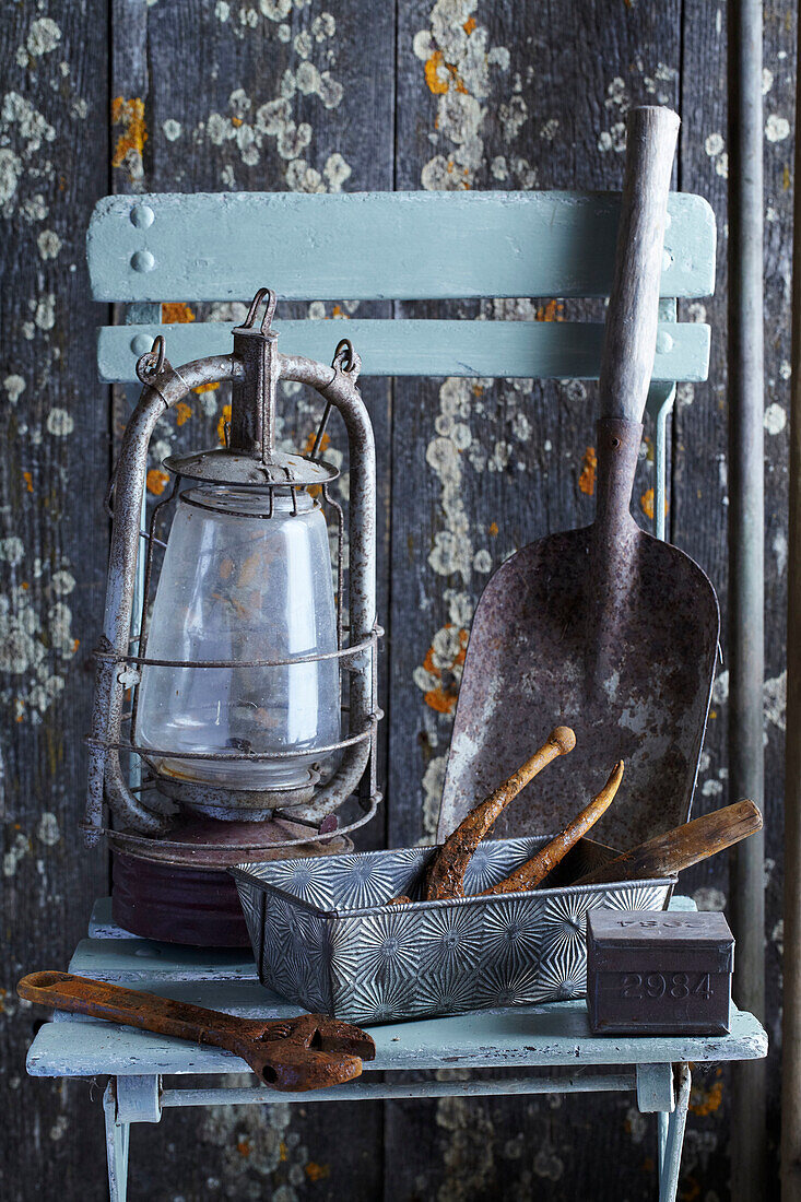 Old gardening tools and paraffin lamp on wooden chair in front of weathered wall