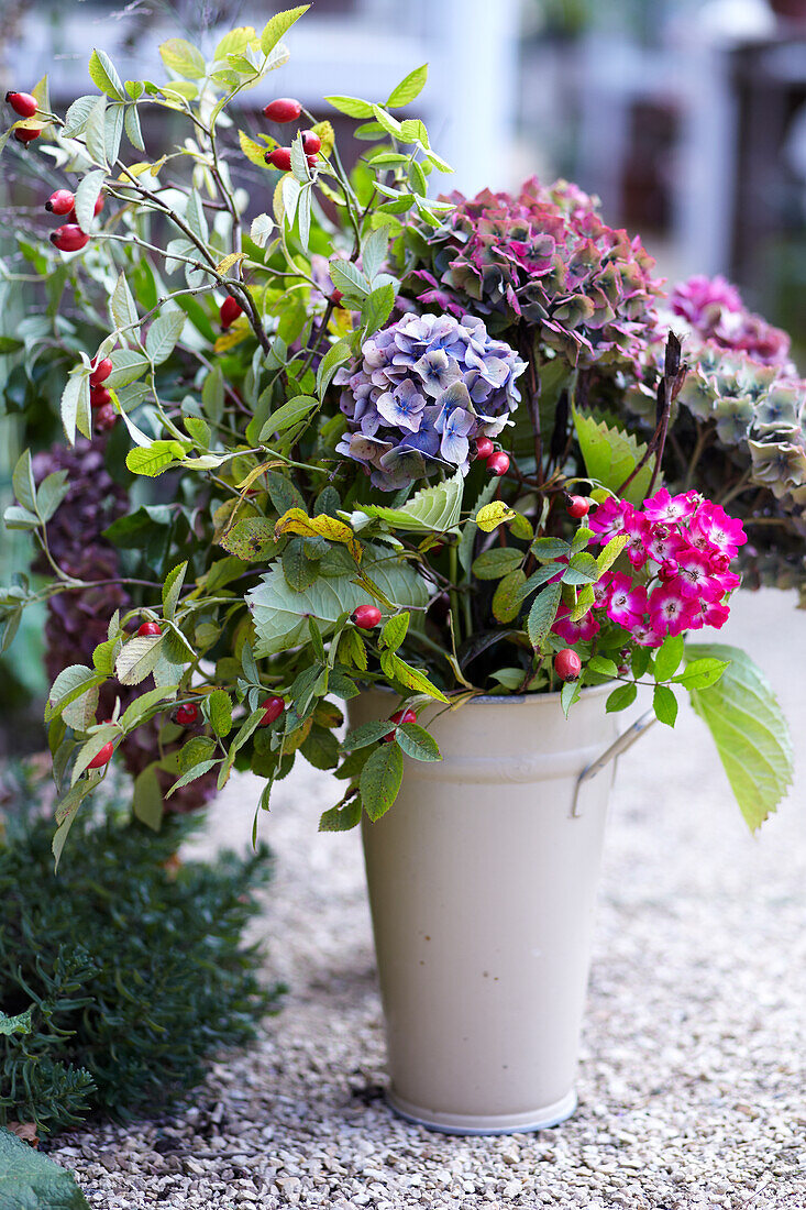 Flower arrangement with hydrangeas and berries in a vase on a gravel path