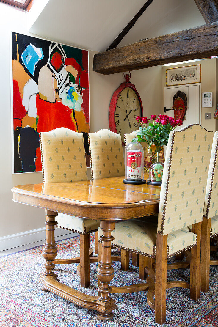 Handcrafted dining table, upholstered chairs with high backrests and modern artworks on wall in the background