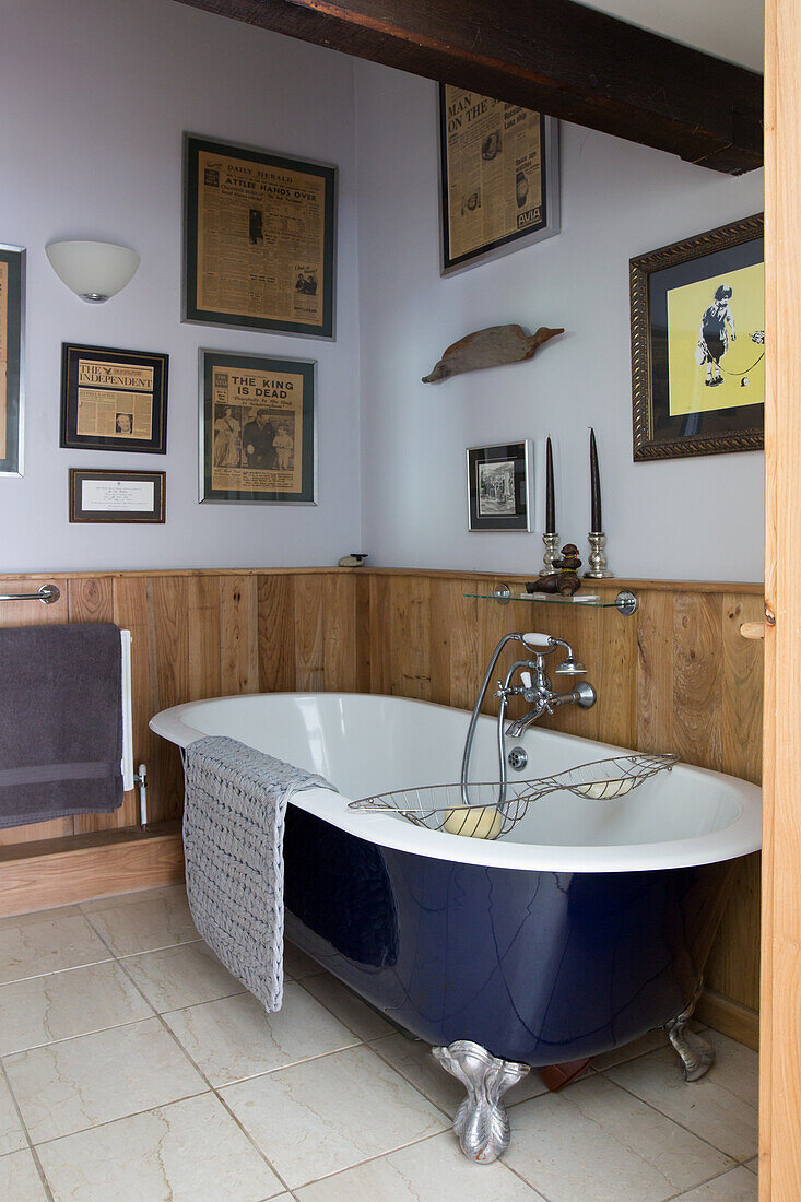Vintage Badewanne im Badezimmer mit niedriger Holzverkleidung und alten, gerahmten Zeitungen