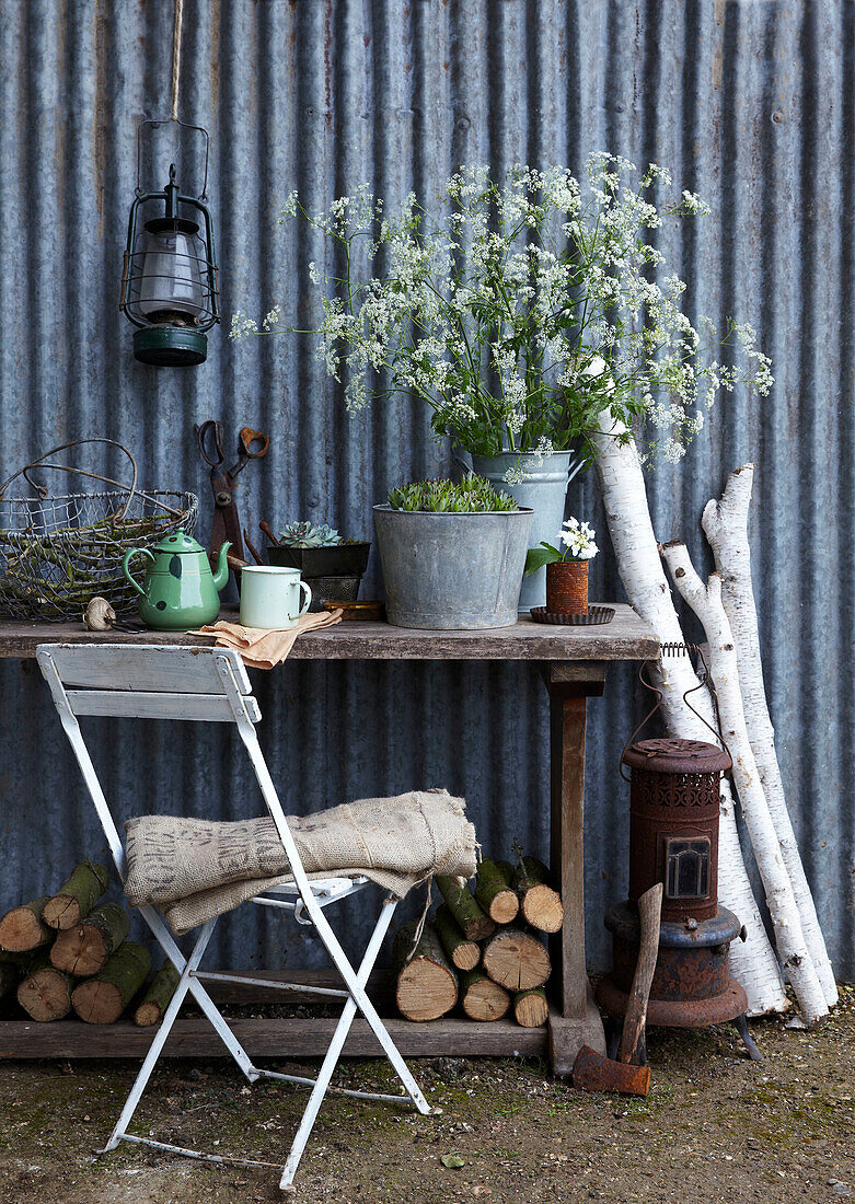 Rustikaler Gartentisch mit Blumen, Ästen und antiker Laterne an der Wand