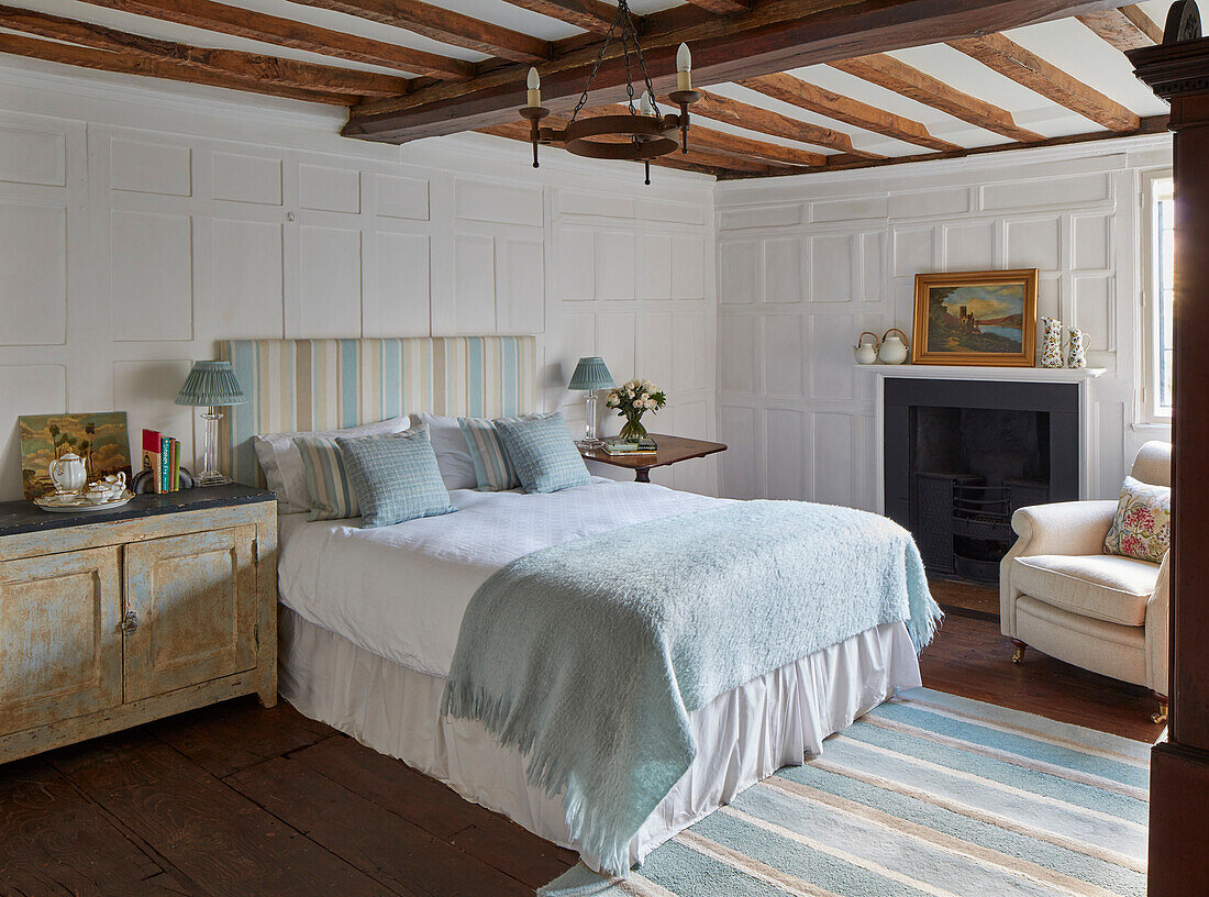 Doppelbett, Nachtschränckchen und Kamin im Schlafzimmer mit Kassettenvertäfelung und Holzbalkendecke