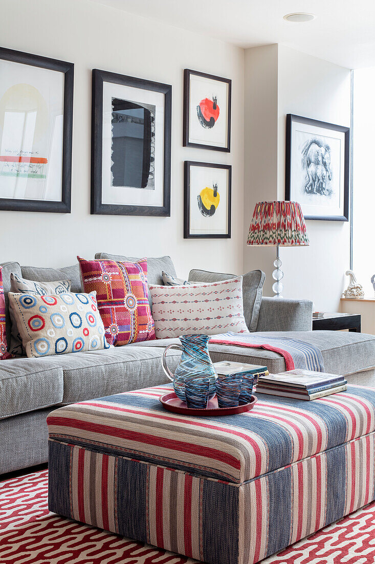 Ottoman with striped cover, sofa with throw pillows and a gallery wall with modern, abstract art collection