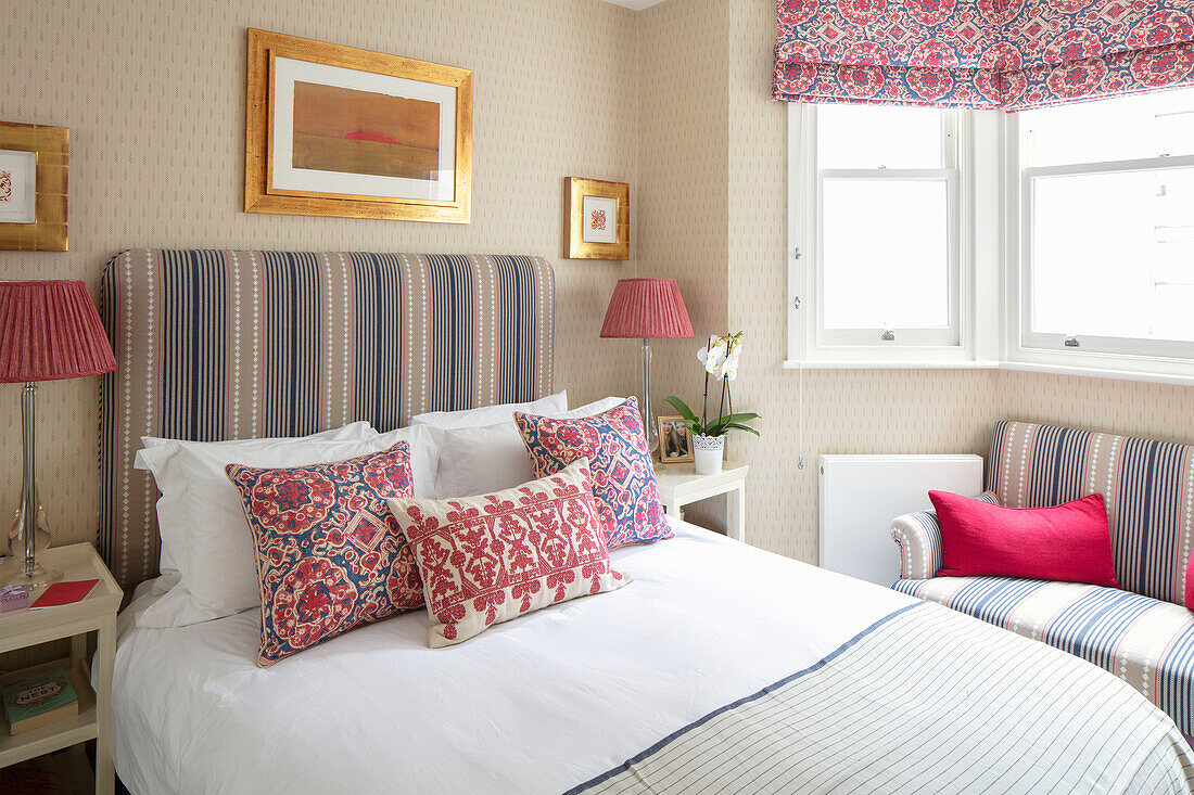 Doppelbett mit Kissen und hohem Betthaupt, Bilder in Goldrahmen an tapezierter Wand