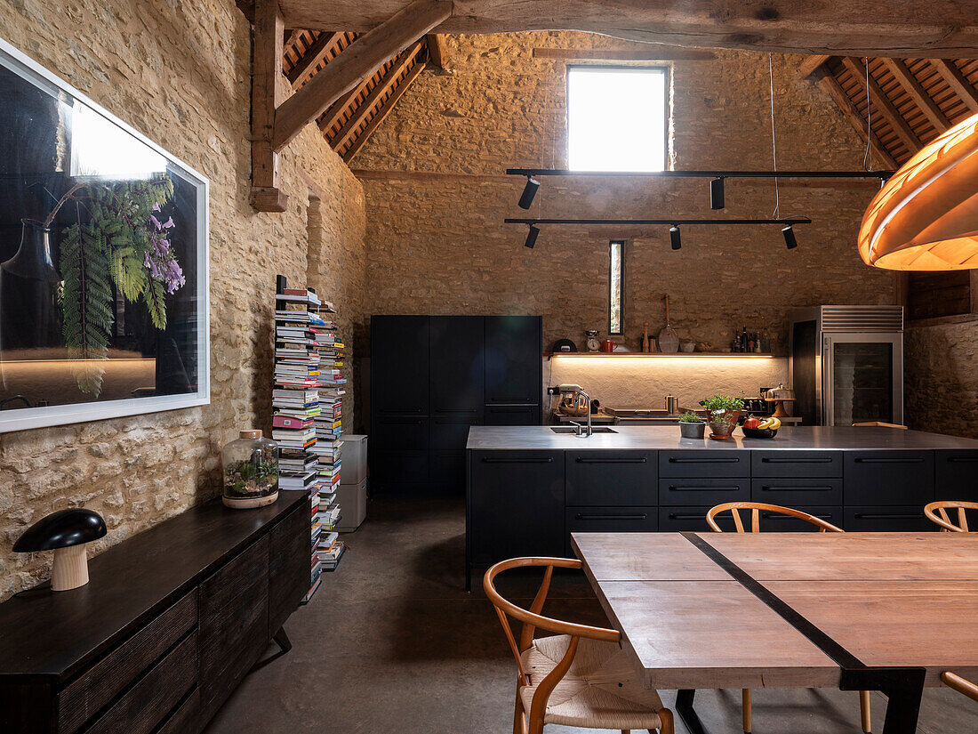 Offene Küche mit großem Esstisch in ehemaliger Scheune mit Natursteinwänden