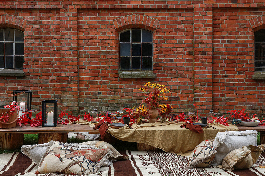 Autumnal picnic table and kilim rug with cushions outside brick house in garden