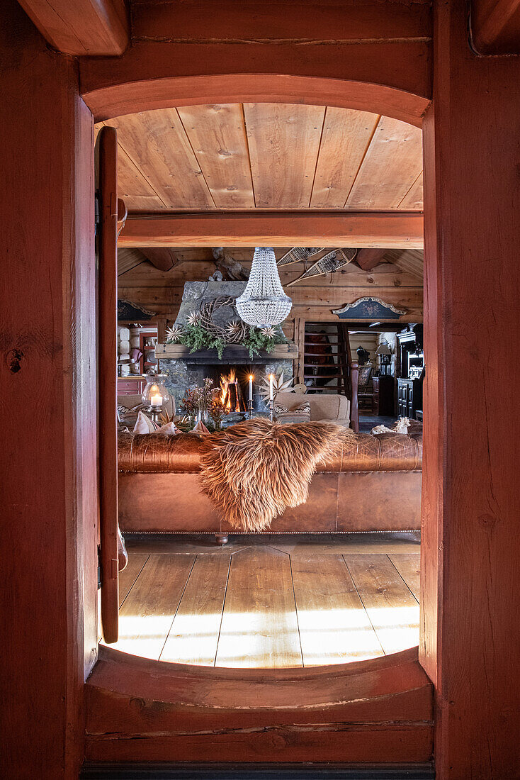 Blick durch rustikale Holztür auf gemütliches Wohnzimmer mit Kamin und Felldeko