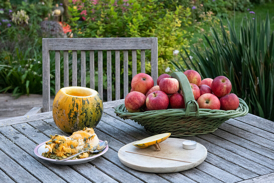 Holztisch im Garten mit Kürbis und Apfelkorb