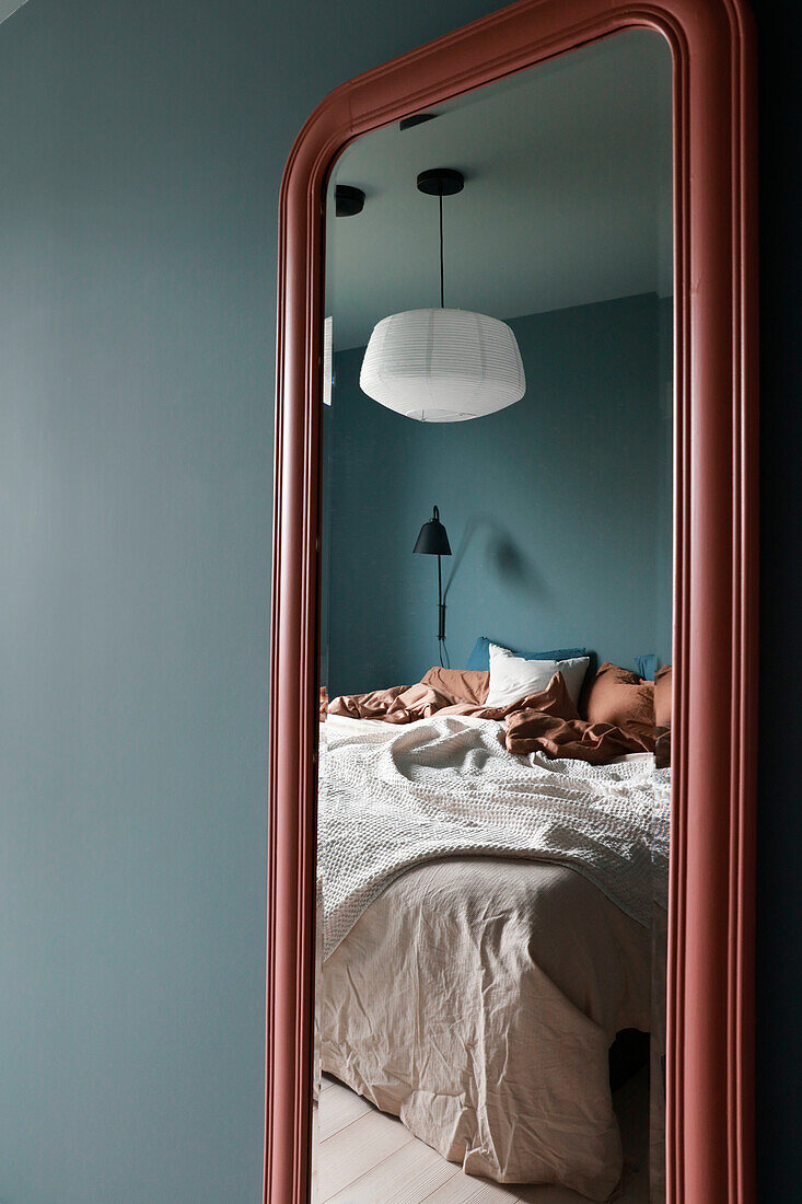 Large mirror in the bedroom with blue-grey walls and bed linen in earthy tones