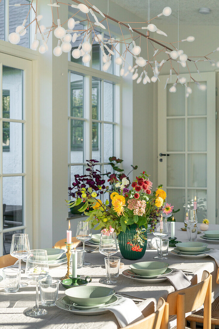 Gedeckter Esstisch mit buntem Blumenstrauß und Hängeleuchte in hellem Raum