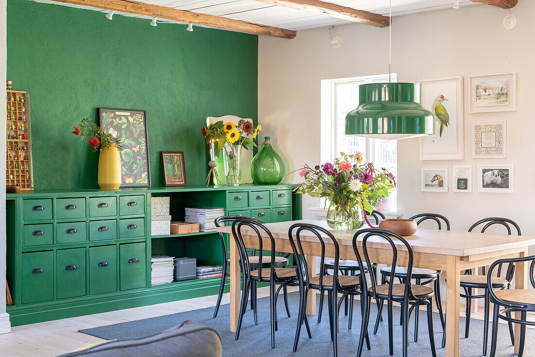 Dining table with chairs in front of green chest of drawers and green wall