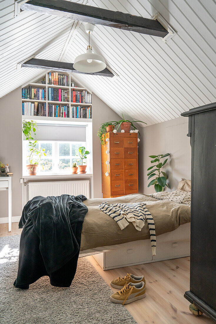 Bedroom under sloping ceilings with bookshelf and plants